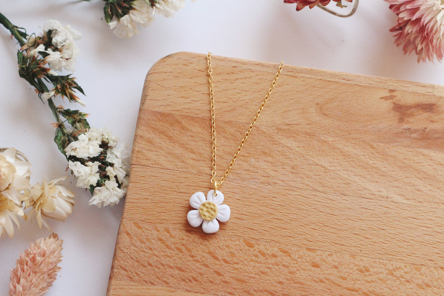 Gold necklace with a white flower pendant on a wooden surface with flowers around