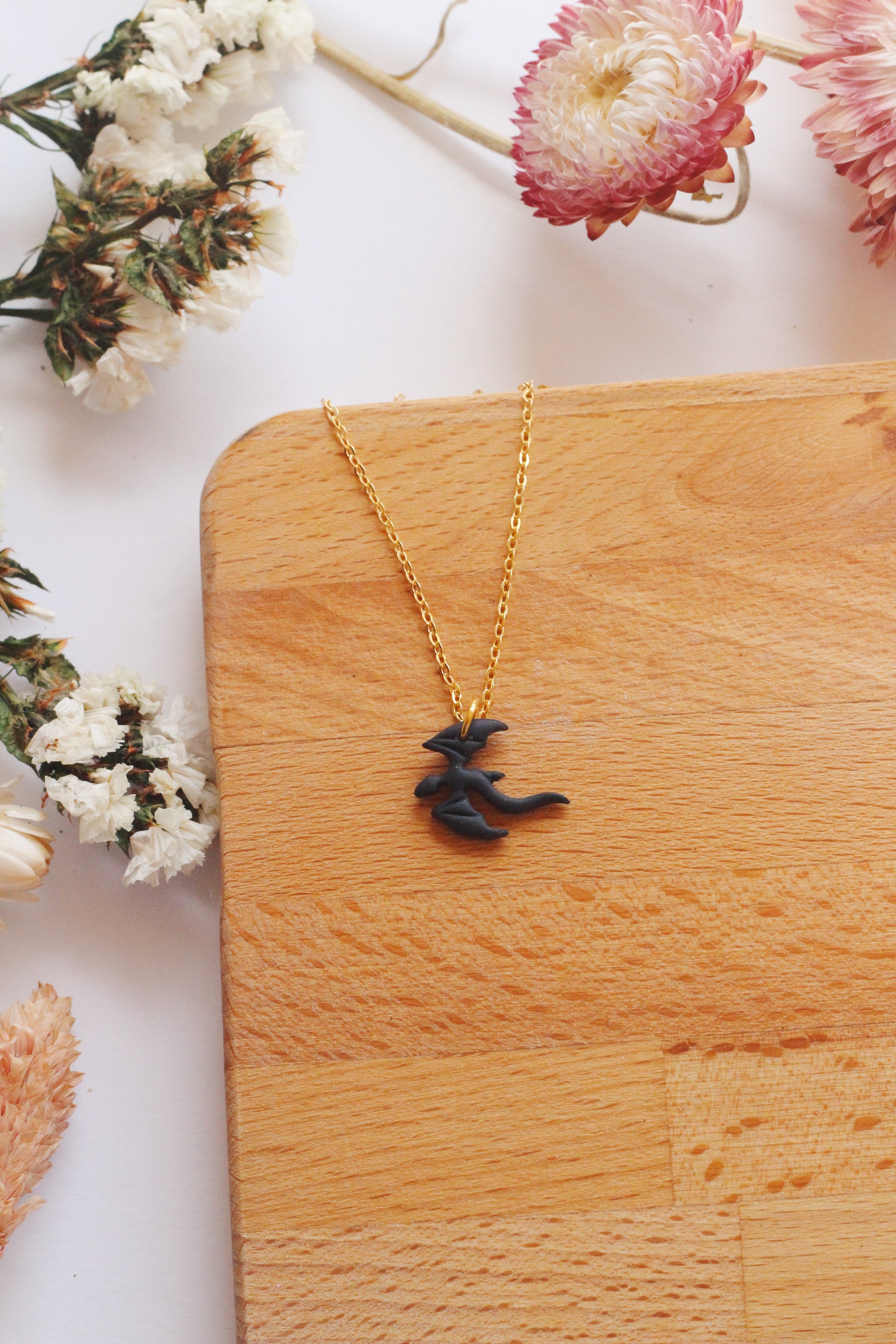 Gold necklace with a black dragon pendant on a wooden surface with flowers around