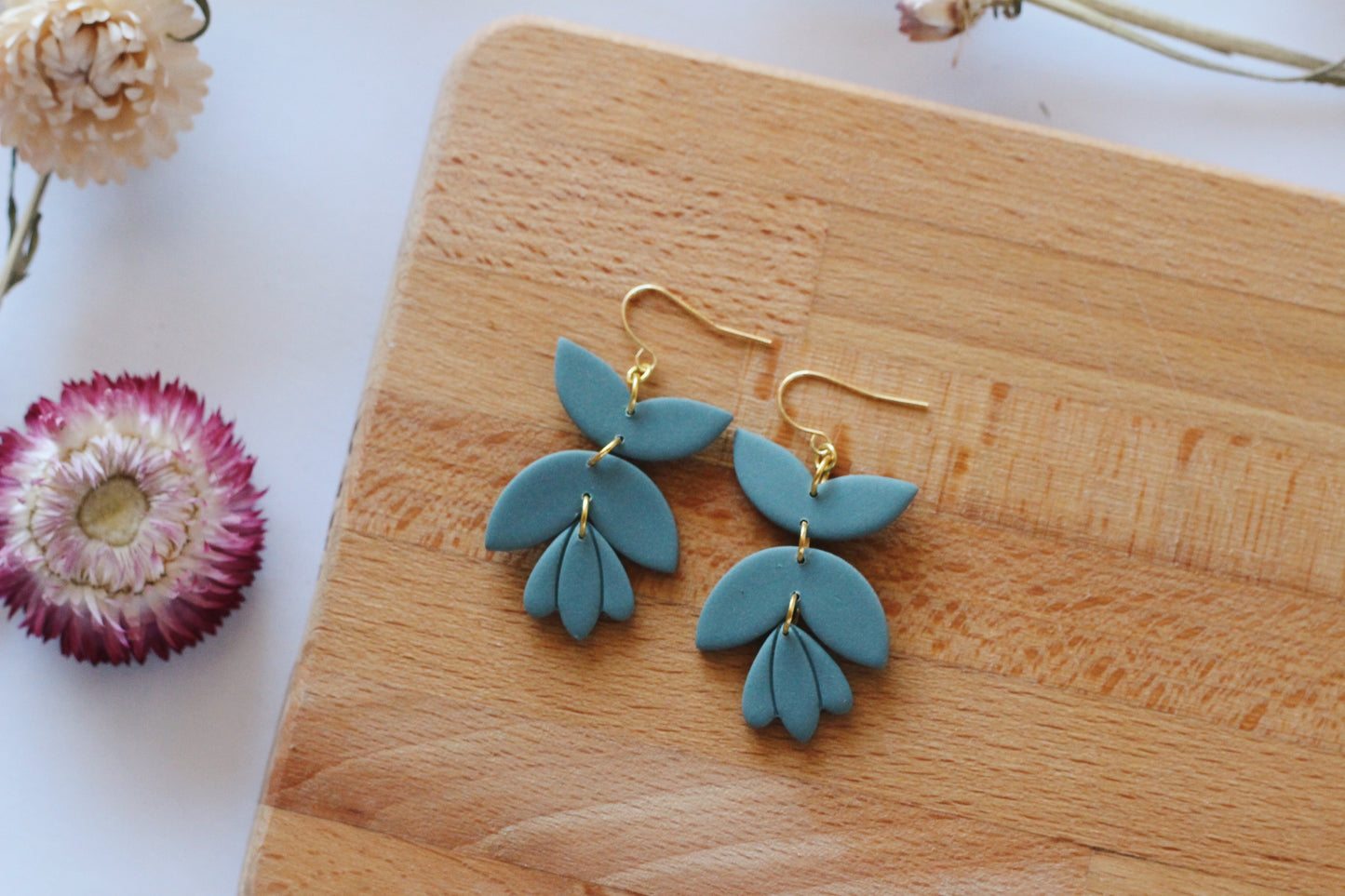 Teal earrings with gold hooks on a wooden surface with dried flowers.
