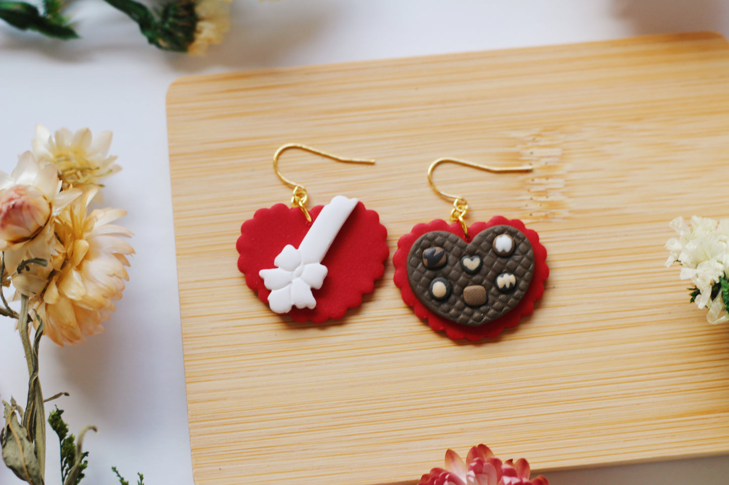 Heart-shaped chocolate box earrings on a wooden board with flowers around