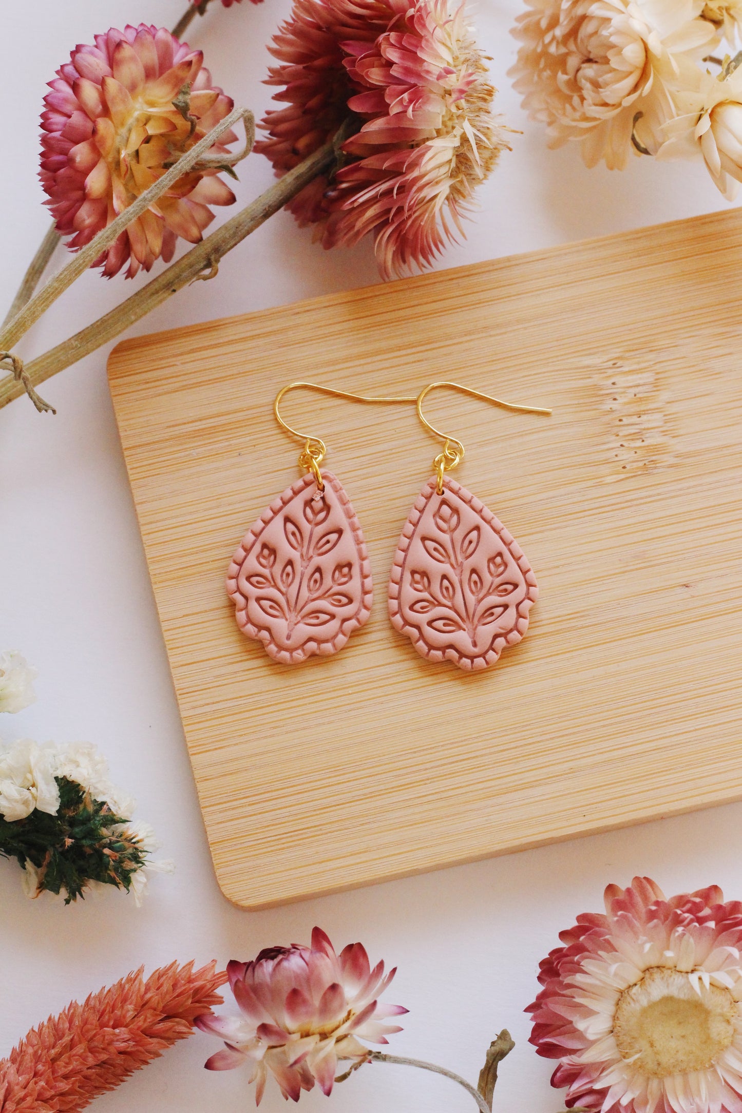 Pink floral earrings on a wooden board with flowers around
