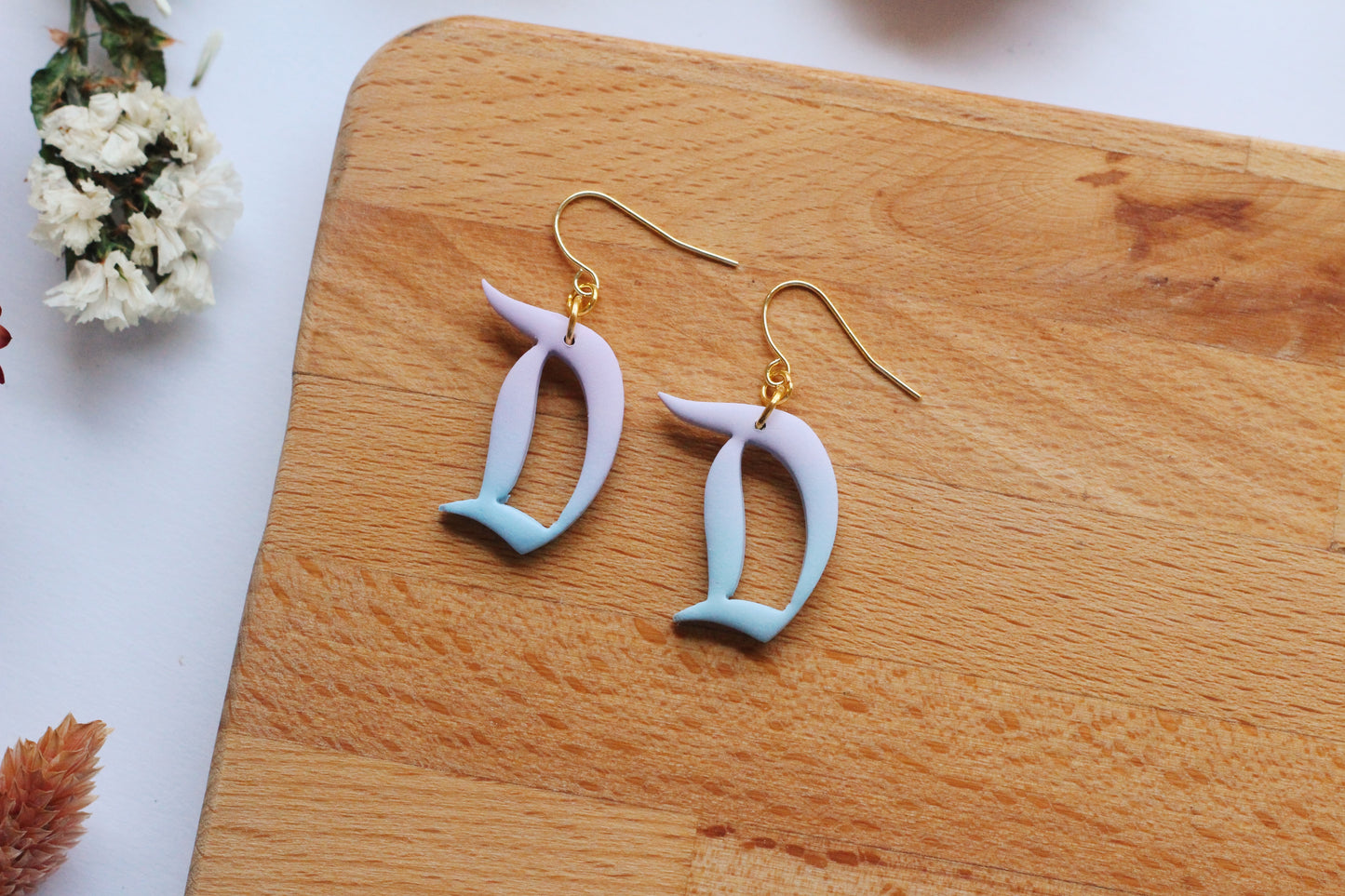 Pair of earrings with 'D' design on a wooden board