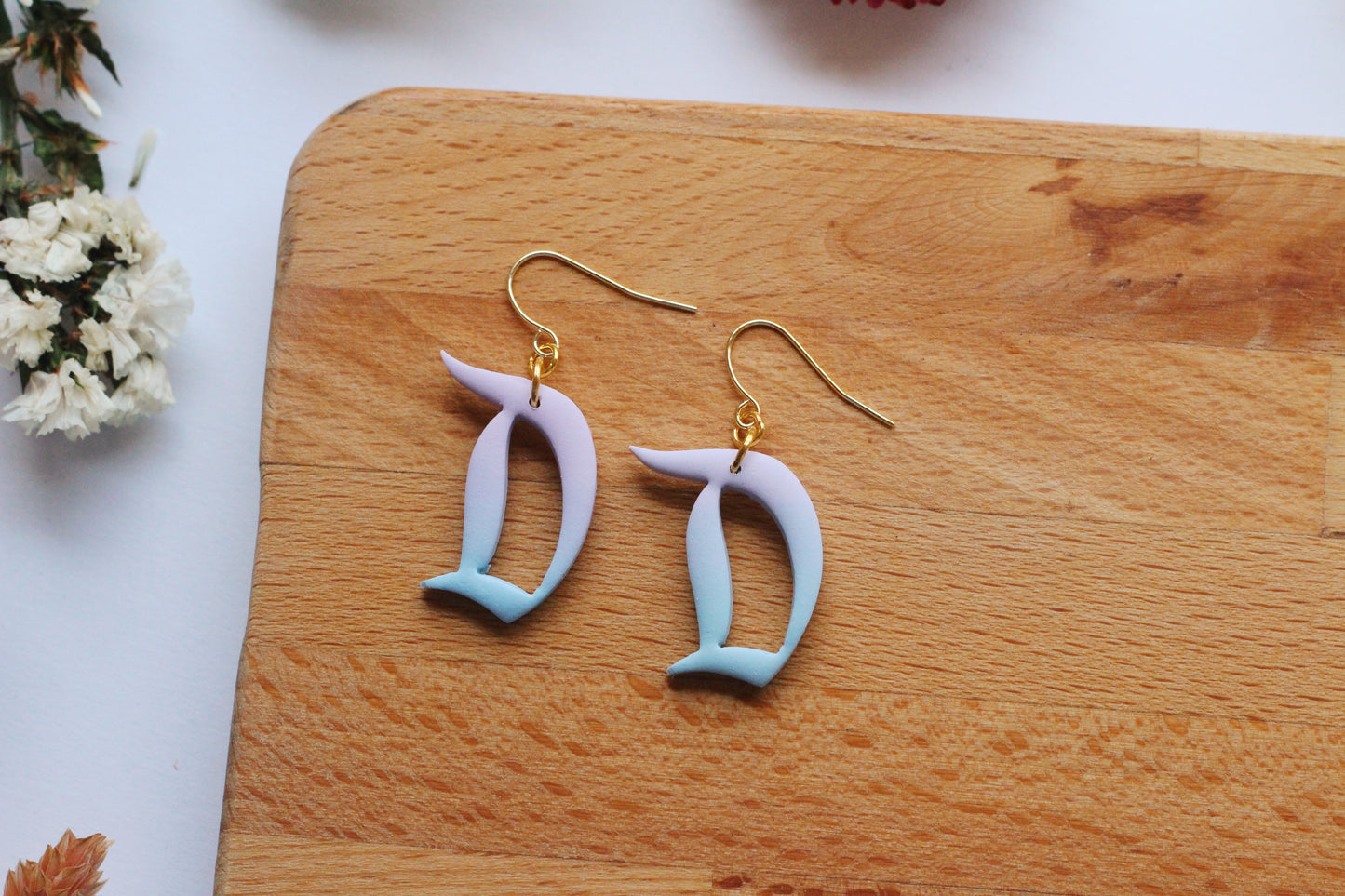 Letter 'D' earrings on a wooden board with flowers in the background