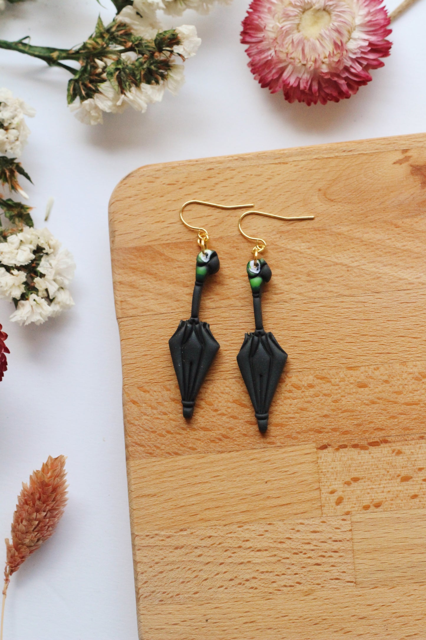 Black umbrella earrings on a wooden board with flowers in the background