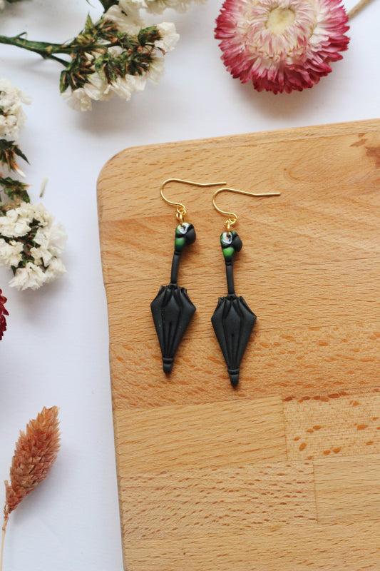 Black umbrella earrings on a wooden board with flowers in the background