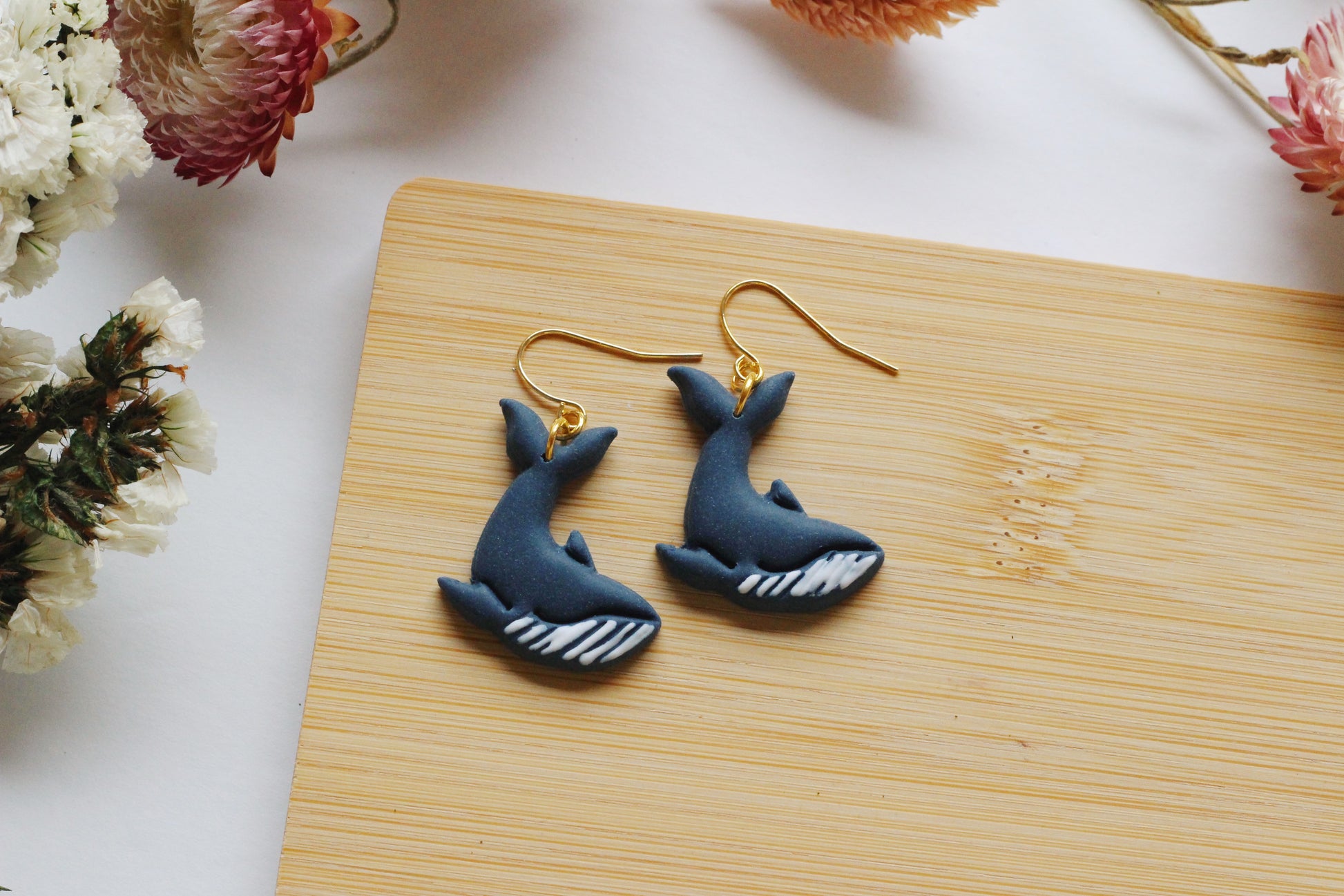 Blue whale-shaped earrings on a wooden surface with flowers in the background