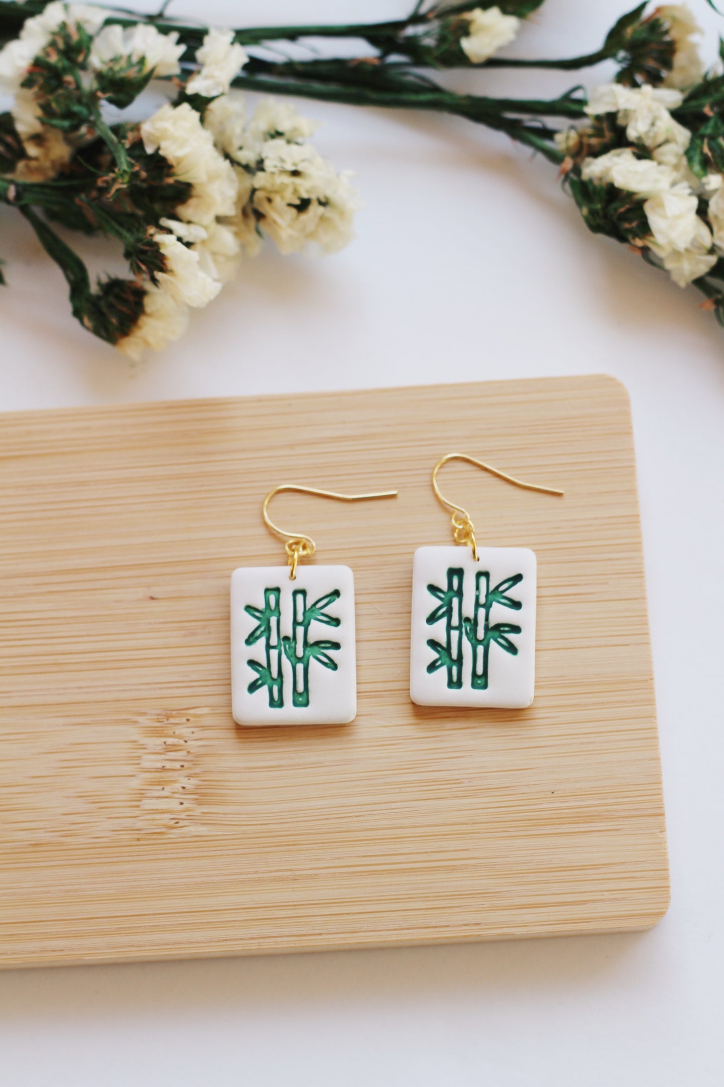 Pair of earrings with green bamboo mahjong tile style, displayed on a wooden board