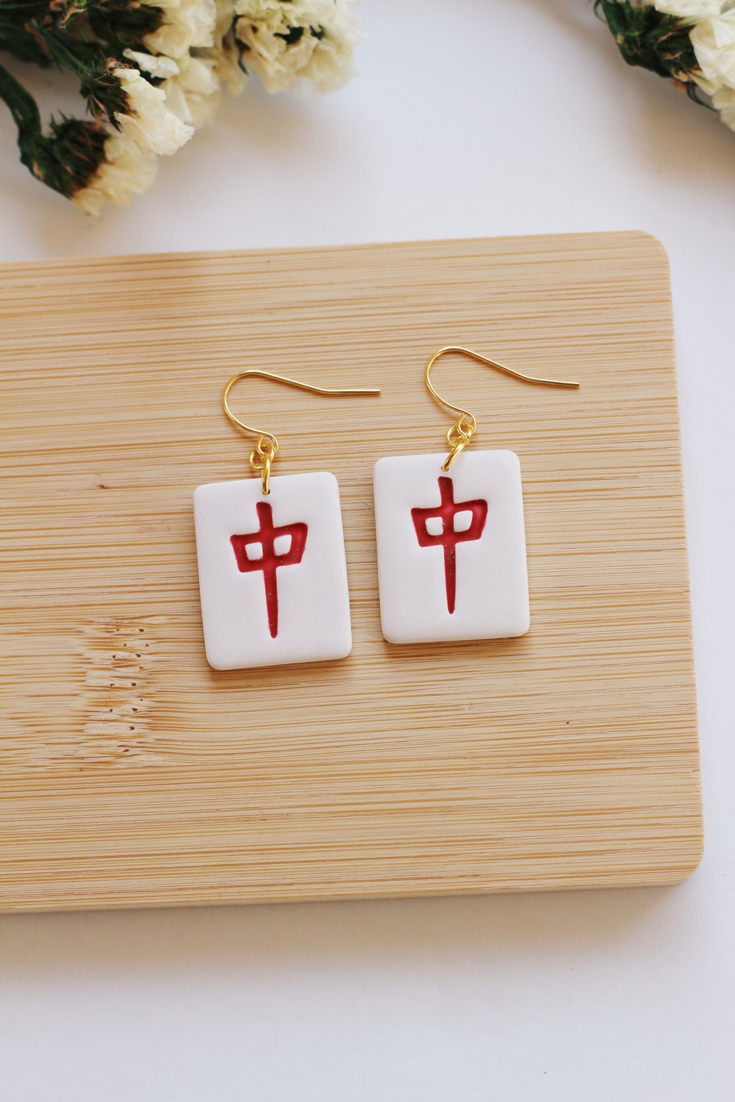 Pair of earrings with red dragon mahjong tile style, displayed on a wooden board