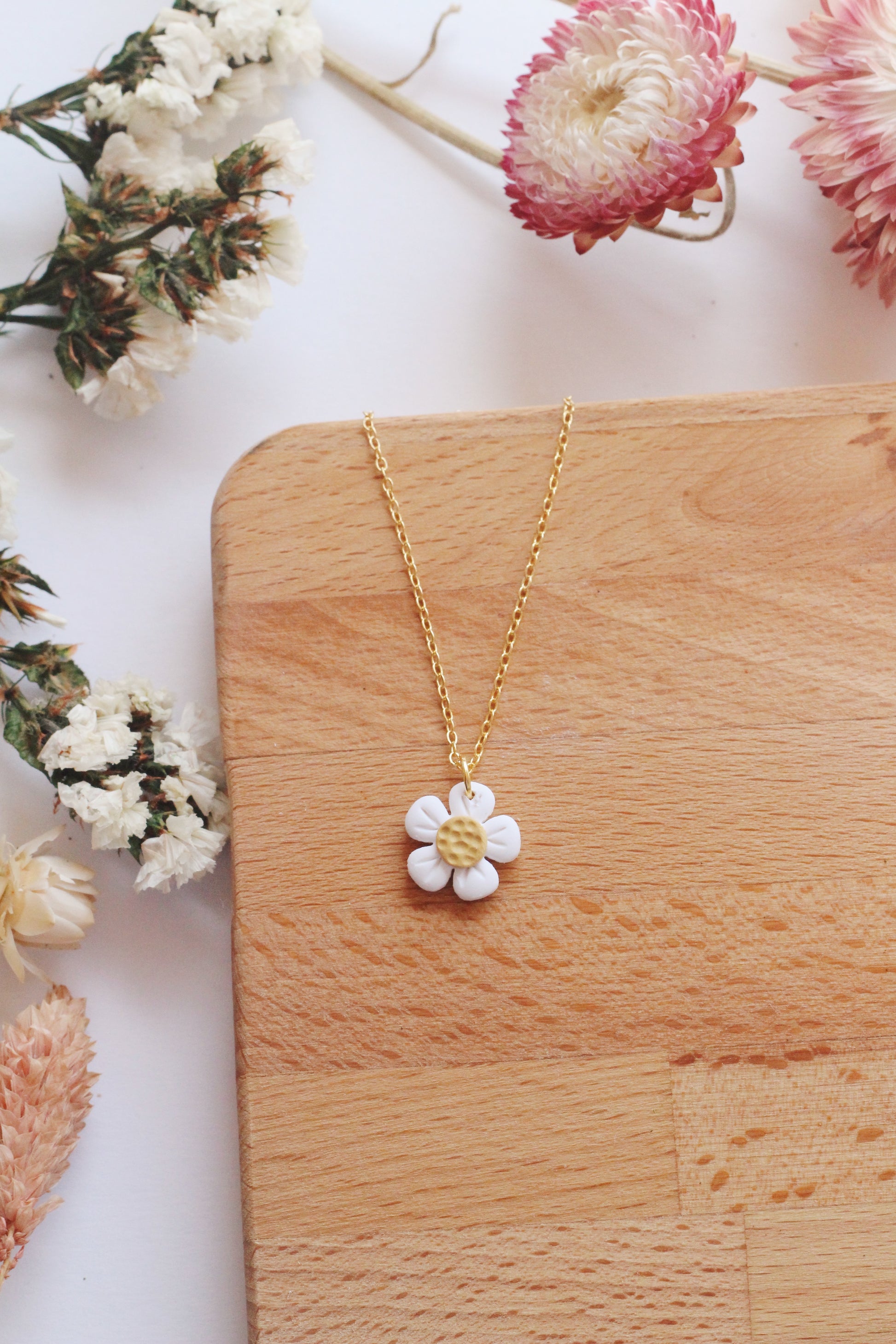 Gold necklace with a white flower pendant on a wooden surface with flowers around