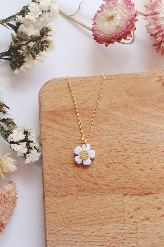 Gold necklace with a white flower pendant on a wooden surface with flowers around