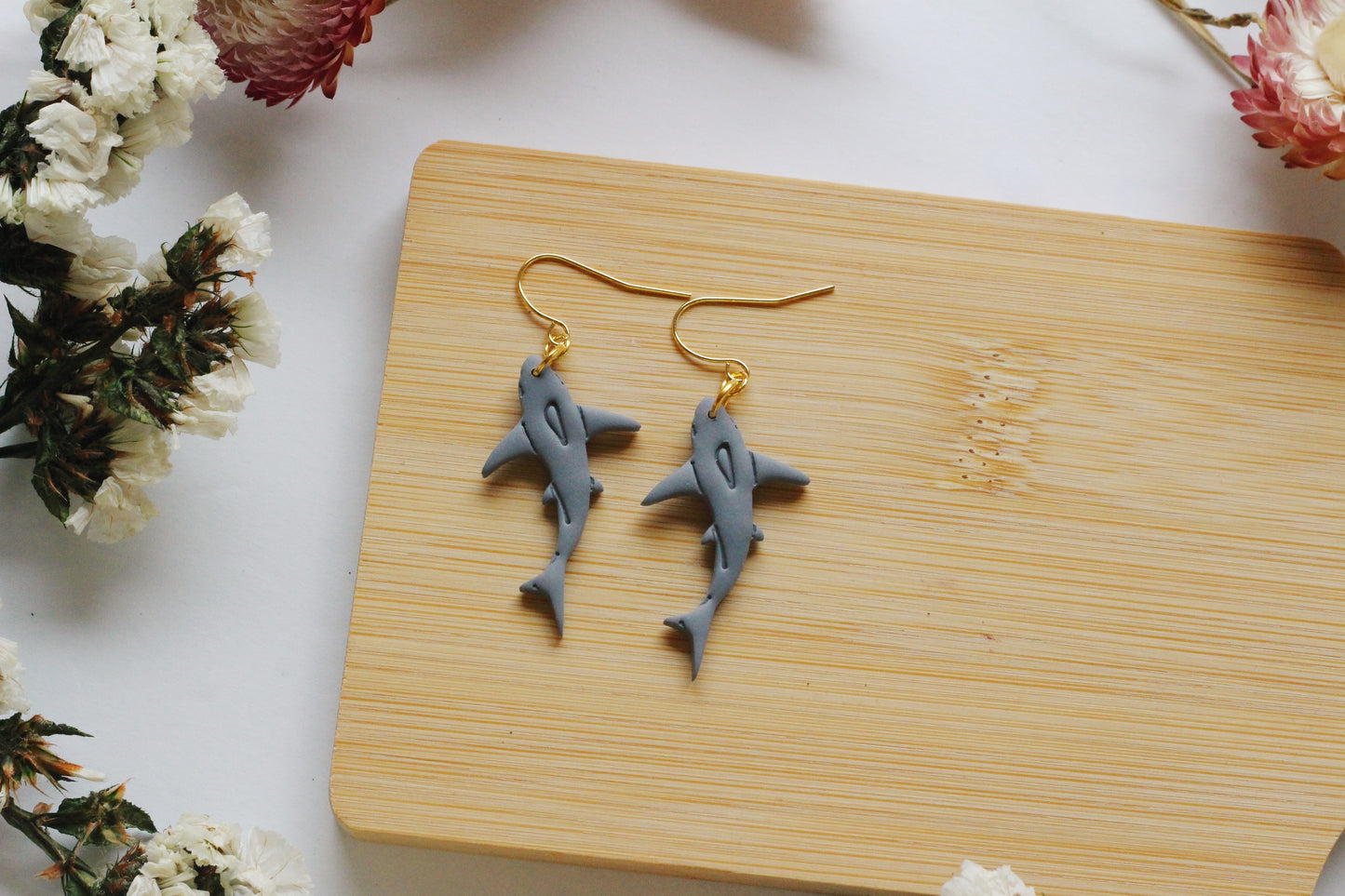 Shark-shaped earrings on a wooden board with flowers around