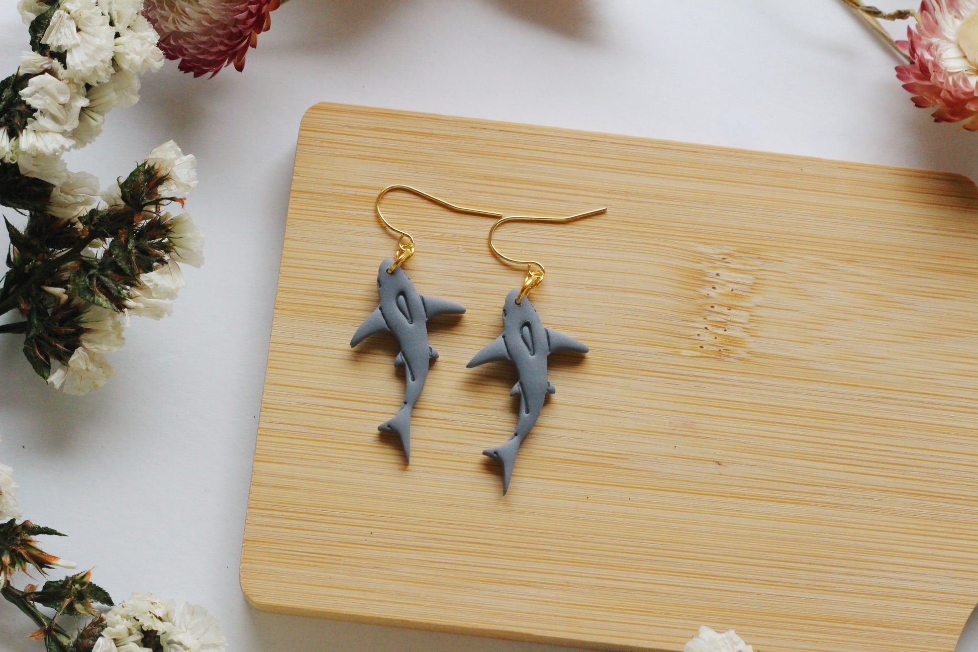 Shark-shaped earrings on a wooden board with flowers around
