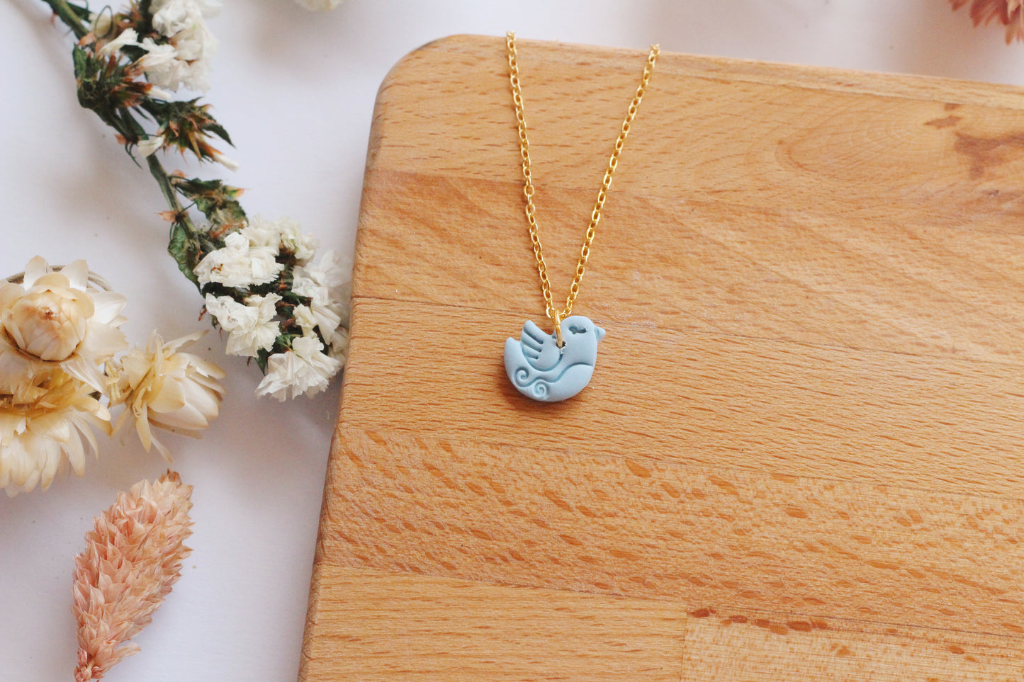 Necklace with a blue bird pendant on a wooden surface with flowers
